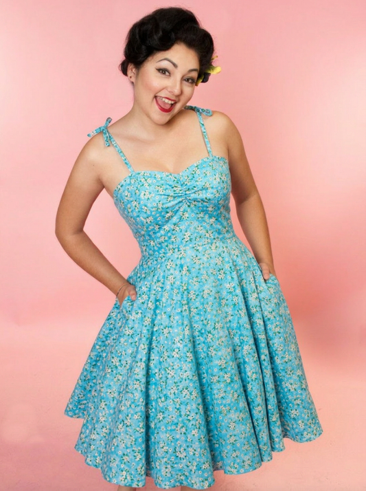 Woman wearing a blue floral dress with thin strap against a pink background