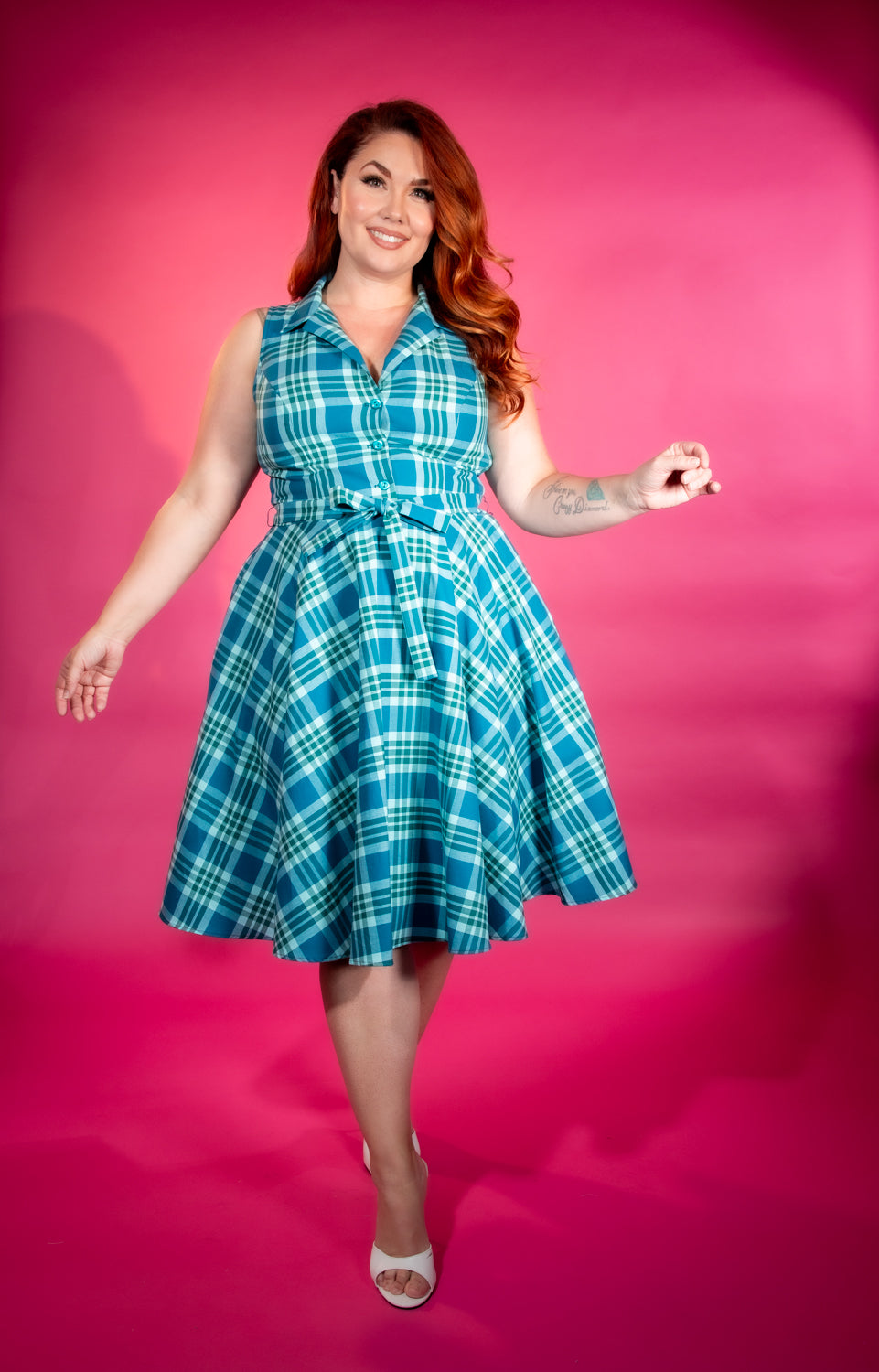 Woman wearing a teal blue plaid dress against a pink background