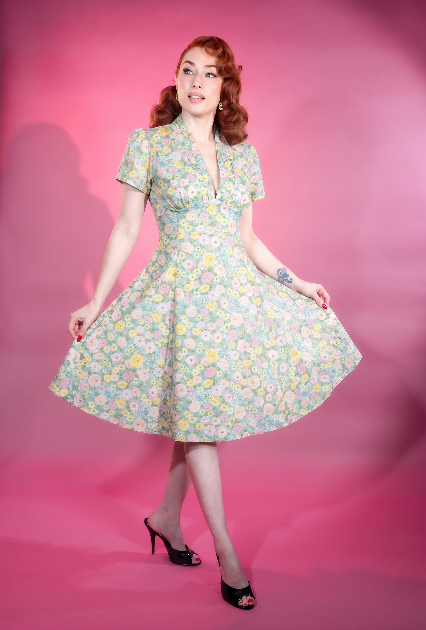 Woman wearing a floral dress against a pink background vintage retro pinup 1950s 1960s style midi dress