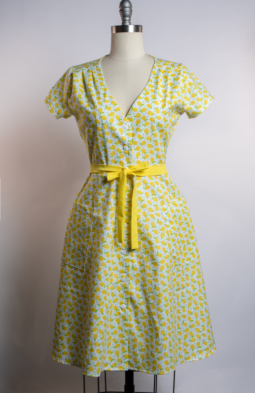 Yellow lemon patterned dress with a yellow belt on a mannequin against a white background